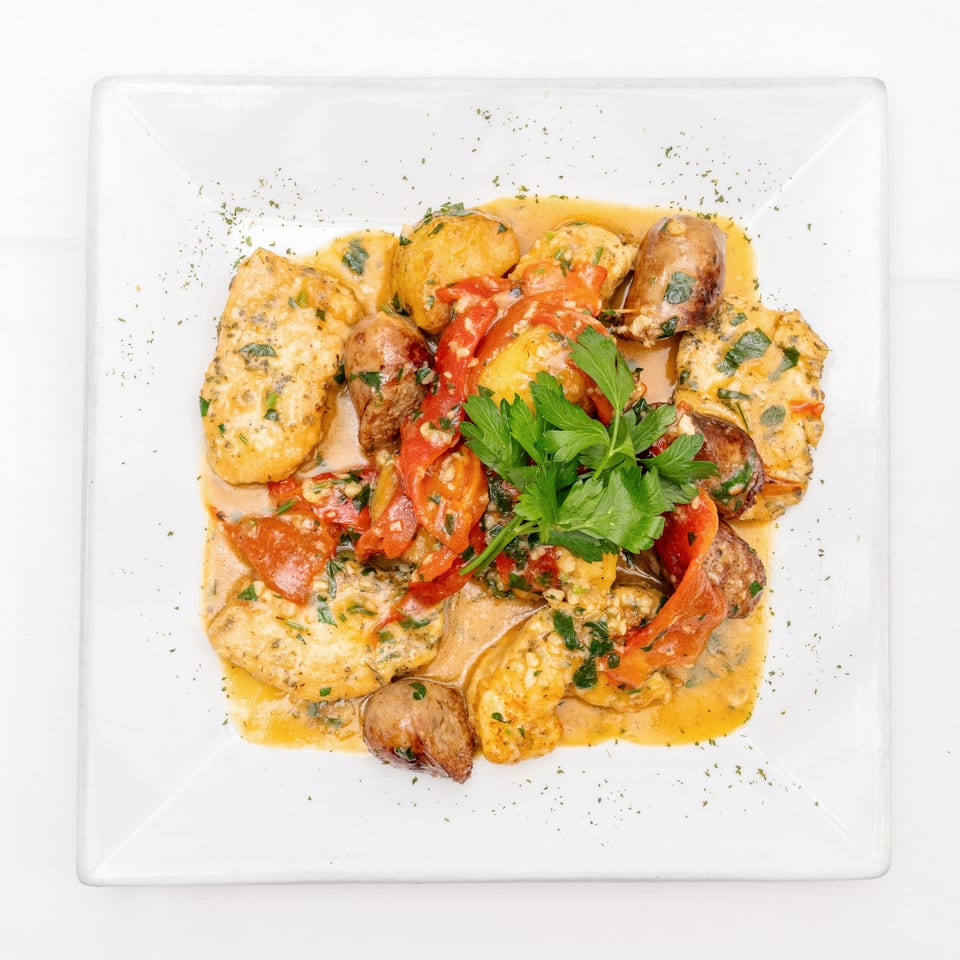 Creamy chicken and sausage dish with potatoes, roasted red peppers, herbs, and parsley on a white plate.