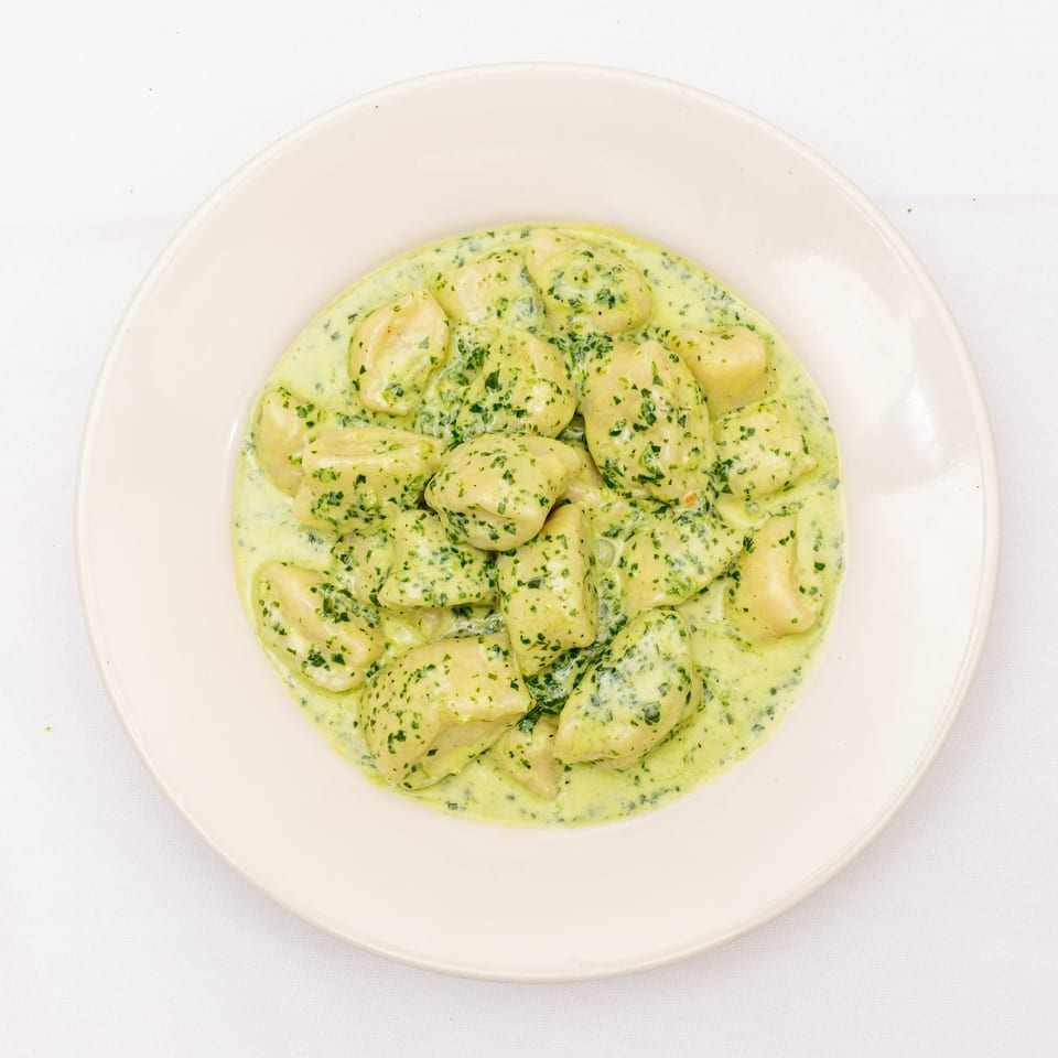 Gnocchi served in a creamy herb sauce on a white plate.
