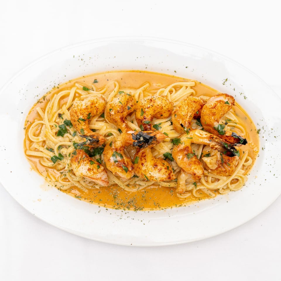 Grilled shrimp and scallops over linguine in a creamy orange sauce, garnished with fresh parsley on a white platter.
