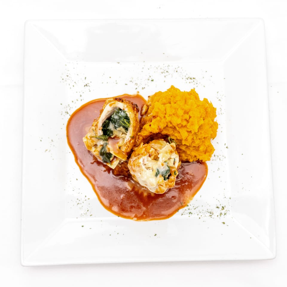 Stuffed chicken breast with spinach filling, orange mashed sweet potatoes, and brown sauce on a white plate.