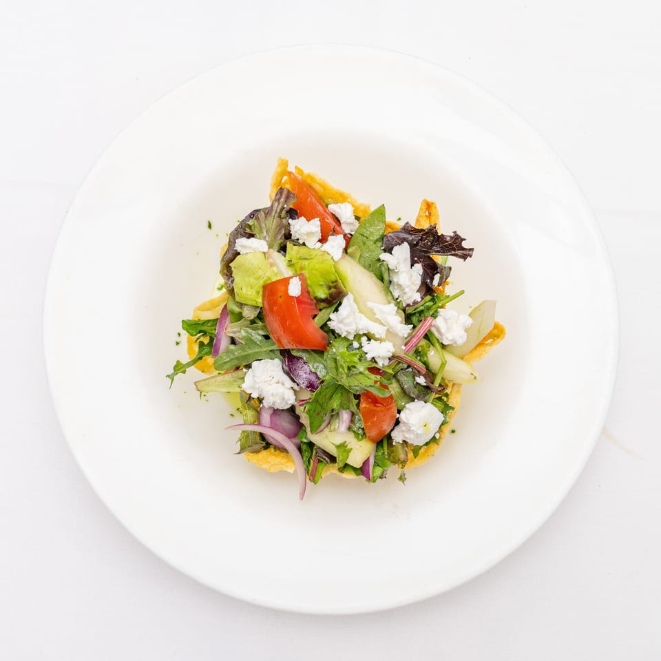 Mixed green salad with tomatoes, cucumbers, red onions, and crumbled feta served on a crisp pastry base.