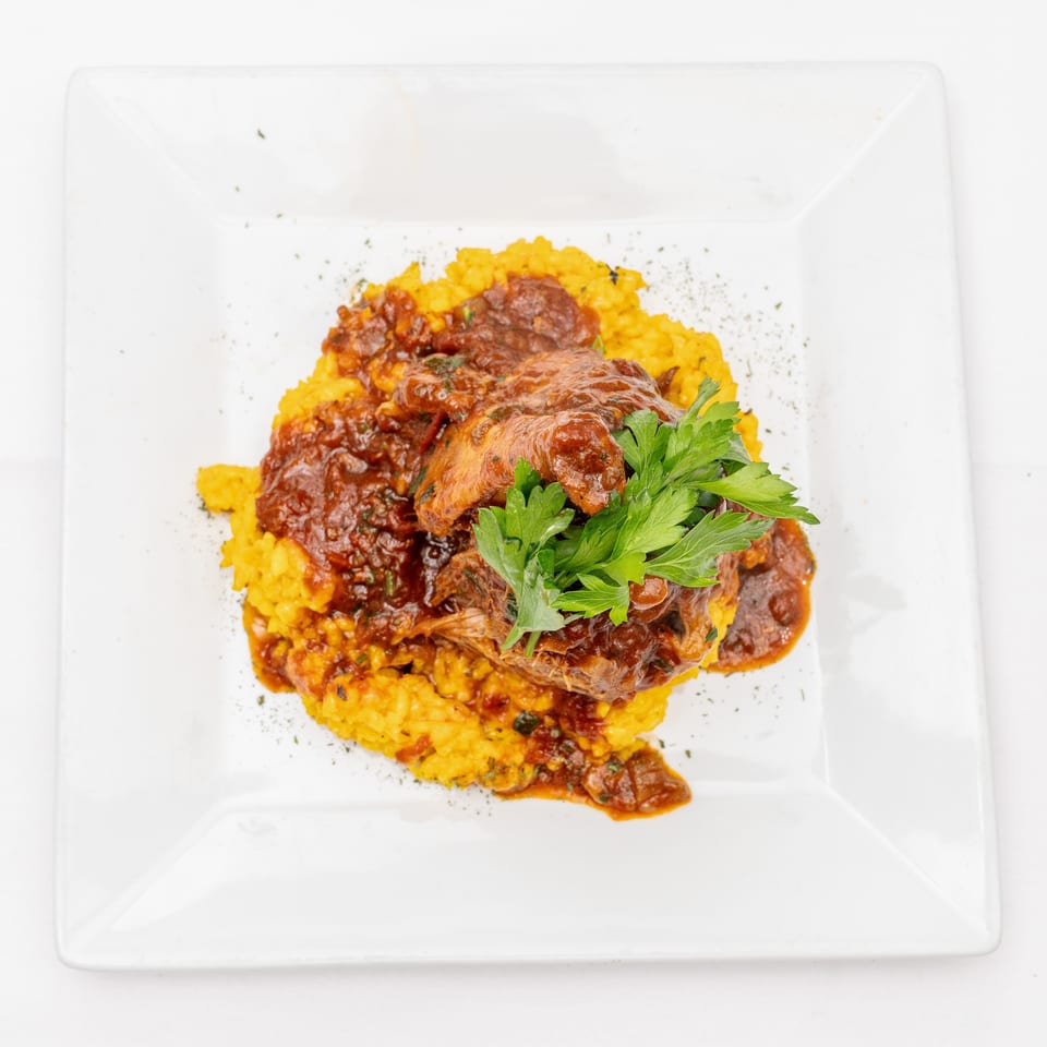 Braised meat in rich sauce served over golden rice and garnished with fresh parsley on a white square plate.