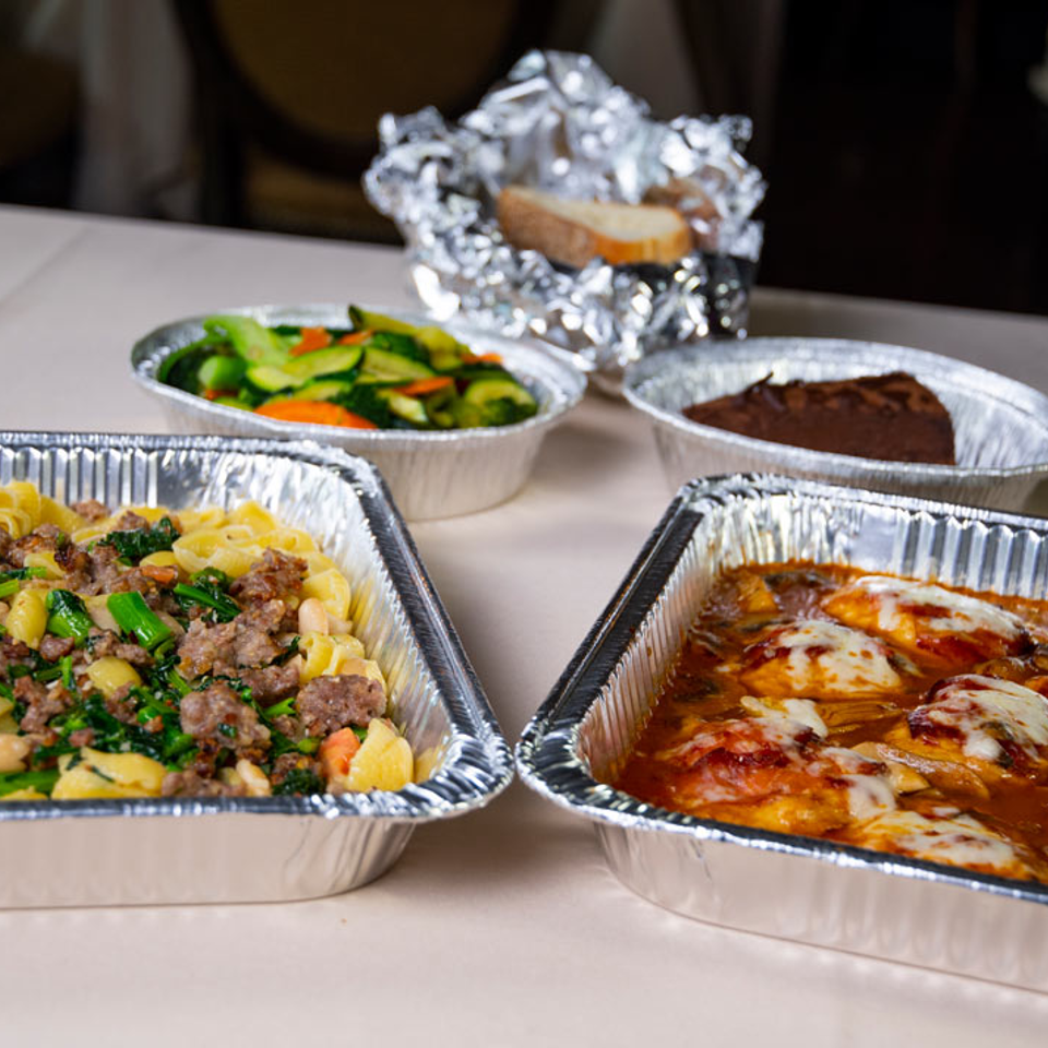 Takeout trays of pasta and chicken with vegetables and dessert